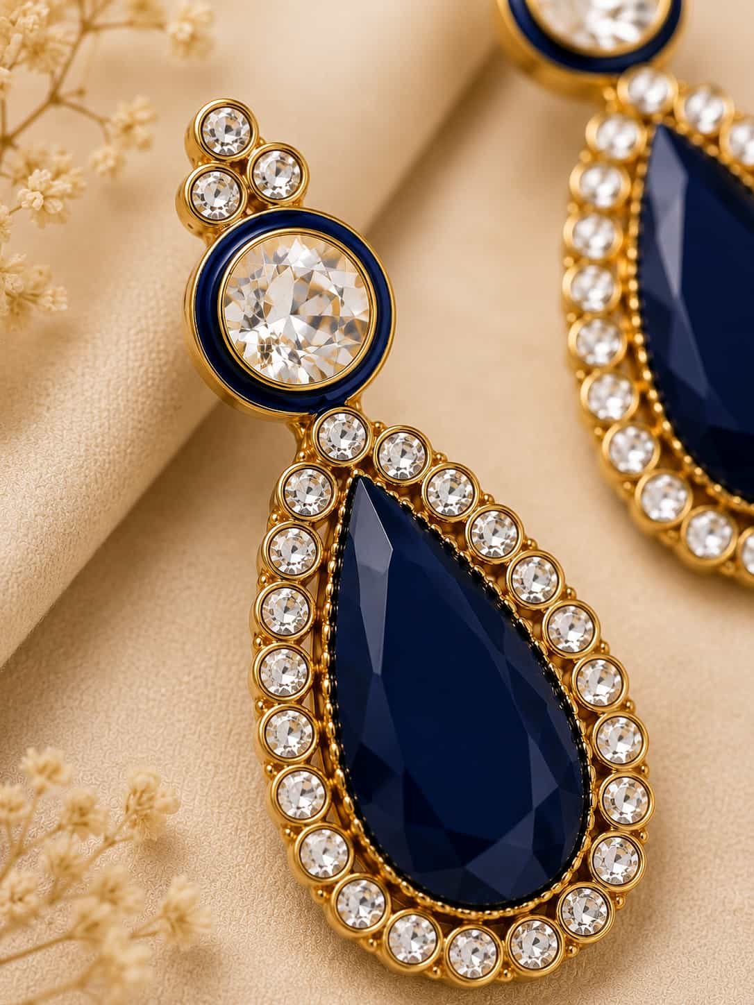 Close-up of Rajneel navy blue teardrop earring with clear stones and gold-tone setting